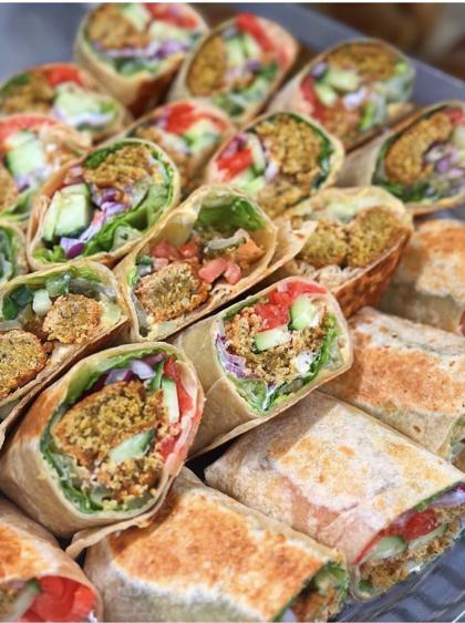 A tray of falafel wraps with salad and tahini, cut and ready to serve